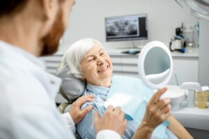 donna anziana sdraiata sulla poltrona del dentista che ride felice dopo aver terminato un intervento per inserire gli impianti dentali a carico immediato