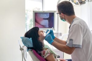 ragazza seduta sulla poltrona del dentista mentre il clinico le analizza bocca e denti con telecamera intraorale